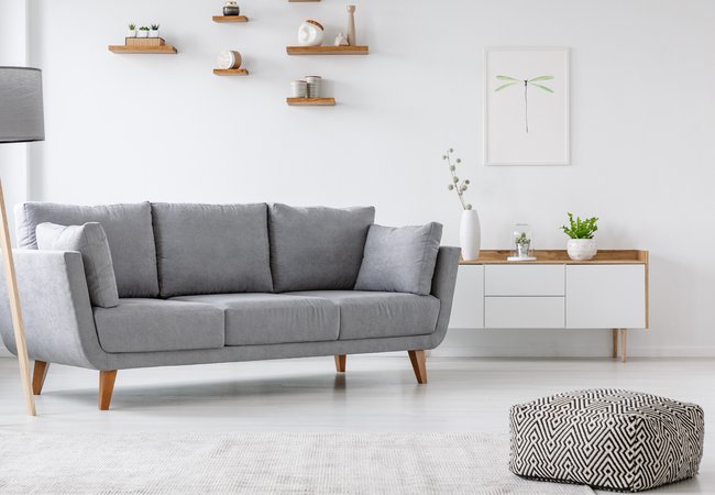 Patterned pouf and grey couch in minimal living room interior with poster above cupboard.